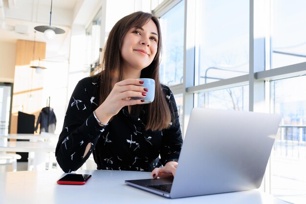 Brunetka pije kawę i pracuje na laptopie w kawiarni