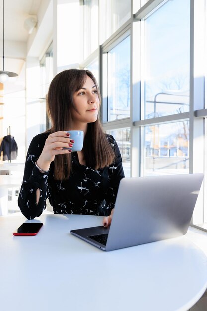 Brunetka pije kawę i pracuje na laptopie w kawiarni