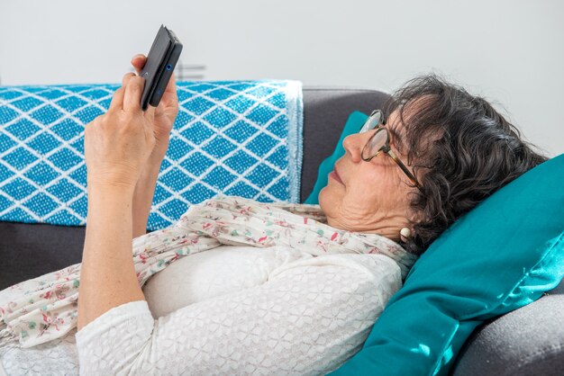 Brunetka starszy kobieta za pomocą smartfona leżąc na kanapie