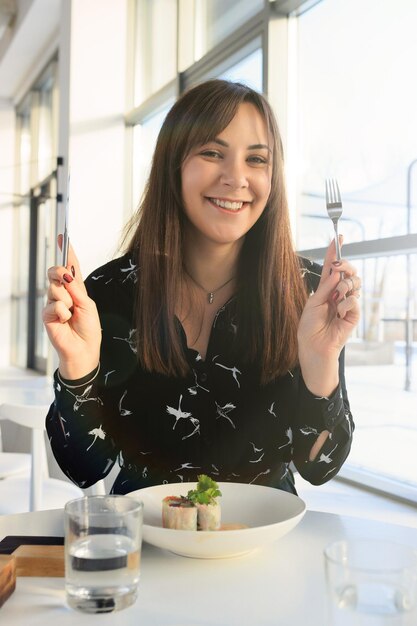 Brunetka w czarnej sukience je w kawiarni Stylowa kobieta podczas lunchu w kawiarni