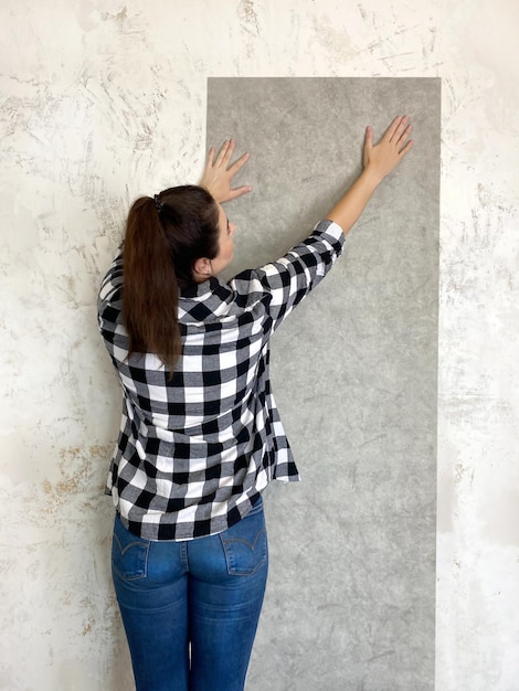 Zdjęcie brunetka wypróbowuje w domu nową tapetę na nowo pomalowanej białej ścianie, aby uzyskać efekt wizualny