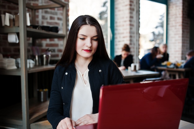 Brunetki dziewczyny obsiadanie na kawiarni i działanie z czerwonym laptopem.