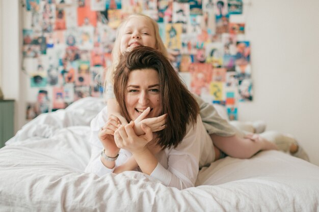 brunetki kobieta z jej piękną szczęśliwą córką bawić się na łóżku
