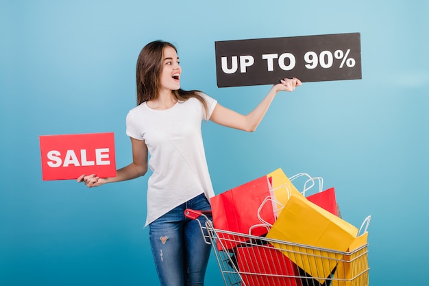 Zdjęcie brunetki kobieta z wózek na zakupy pełen kolorowych czerwonych i żółtych papierowych toreb i 90% sprzedaży znak izolowanych na niebiesko
