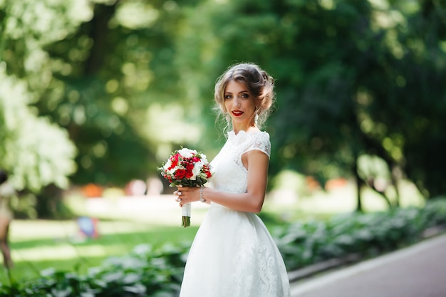 Brunetki panna młoda w sukni z ślubnym bukietem w parku