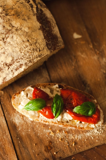 bruschetta z chleba ciabatta z suszonymi pomidorami i liśćmi bazylii na drewnianym tle śniadanie