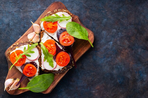 Bruschetta Z Serkiem śmietankowym, Pomidorkami Koktajlowymi I Czosnkiem Na Desce Do Krojenia. Włoskie Antipasti Bruschetta Z Twarogiem I świeżymi Ziołami. Skopiuj Miejsce. Widok Z Góry