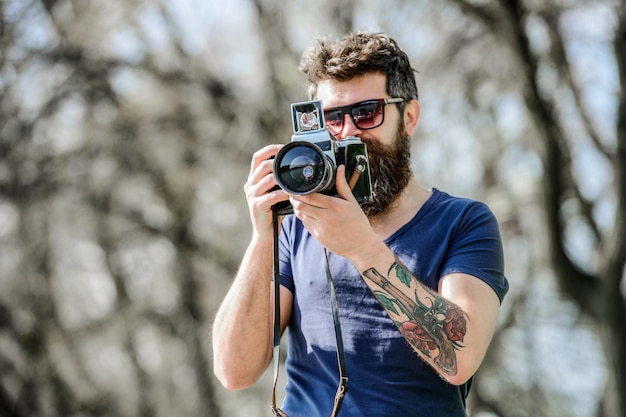 Brutalny fotograf z aparatem zdjęcie natury reporter lub dziennikarz retro sprzęt fotograficzny hipster mężczyzna w letnich okularach przeciwsłonecznych Dojrzały hipster z brodą Profesjonalny fotograf