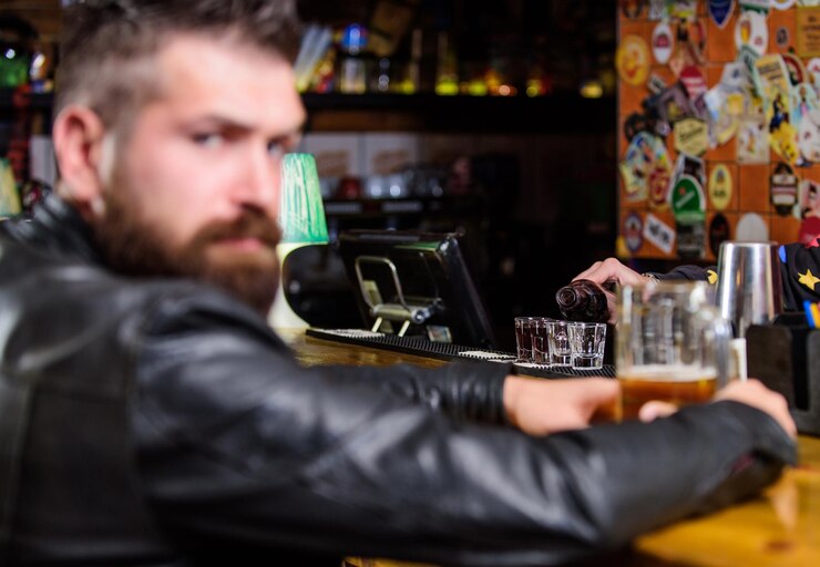 Zdjęcie brutalny hipster brodaty mężczyzna siedzi przy liczniku baru pije piwo w piątek wieczorem bar jest relaksującym miejscem do picia i relaksu mężczyzna z brodą spędza wolny czas w ciemnym barze hipster relaksujący się w barze z piwem