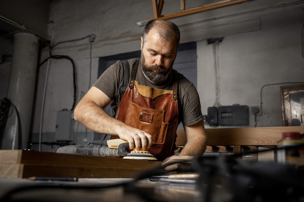Brutalny mistrz stolarski szlifuje drewniane półfabrykaty za pomocą maszyny w warsztacie