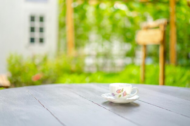 Brytyjski styl filiżanki herbaty z rysunkiem różowego kwiatka na drewnianym ciemnobrązowym stole rano z rozmytym ogrodem i oknem