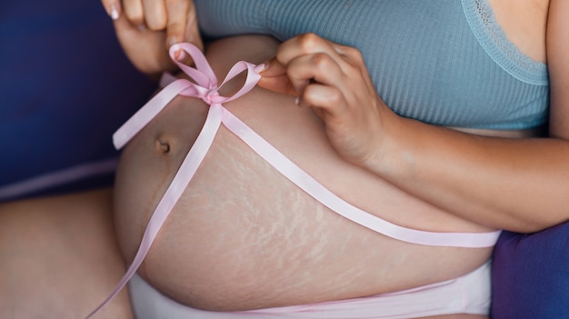 Zdjęcie brzuch ciężarnej dziewczyny z różową wstążką wokół brzucha. zbliżenie na brzuch w ciąży