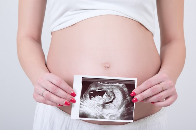 Brzuch młodej kobiety w ciąży z obrazem USG na białym tle