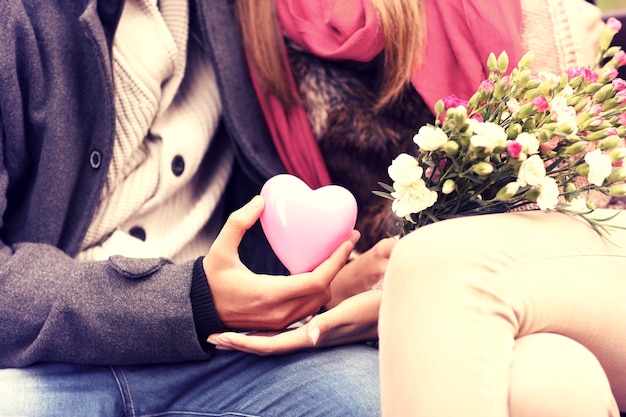 Brzuch romantycznej pary siedzącej na ławce w parku, trzymającej walentynkowy prezent i kwiaty