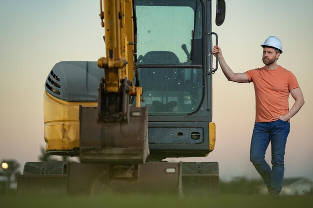 Budowniczy mężczyzna w pobliżu koparki Pracownik budowlany z koparką Konstruktor w kasku Pracownik w kasku Portret pracownika mechanicznego w kasku budowlanym Inżynier brygadzista budowlany lub mechanik