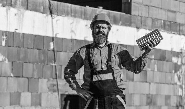 Zdjęcie budowniczy trzyma cegłę brodaty mężczyzna nosi kask na budowie ceglany materiał budowlany używany do budowy ścian lekka cegła wykonana z ekspandowanego kruszywa glinianego element w budownictwie murowym