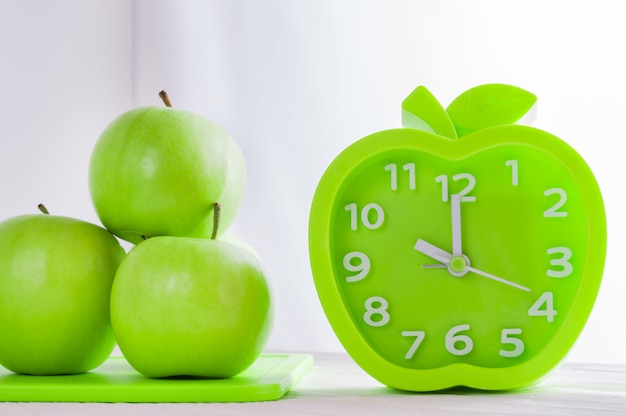 Budzik i zieleni jabłka na białym drewnianym stole. Dzień dobry, zdrowy poranek lub koncepcja diety.