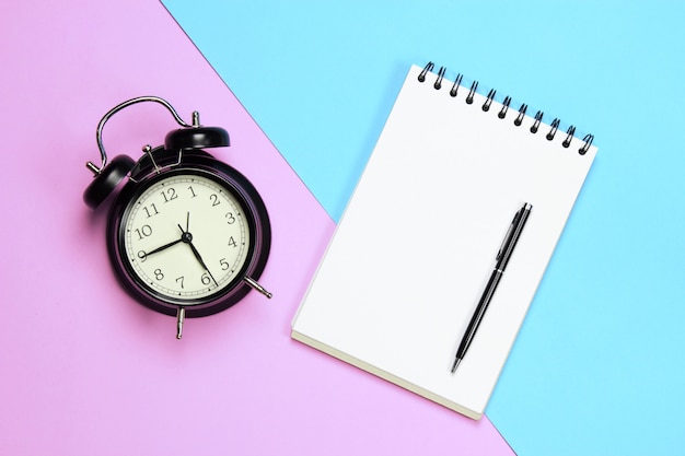 Zdjęcie budzik papierowy długopis na różowym i niebieskim tle w notatniku koncepcji i zrelaksować czas na pracę
