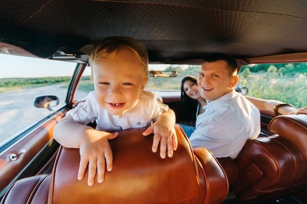 Buick Rivierin w stylu retro. Unikalny samochód. Ładny blond chłopiec siedzi za kierownicą samochodu retro z rodziną