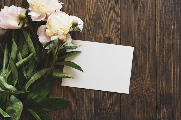 Zdjęcie bukiet białych różowych kwiatów i białej karty na drewnianym tle płaskie leżały minimalistyczne estetyczne piwonie piękna karta na dzień matki lub dzień kobiet