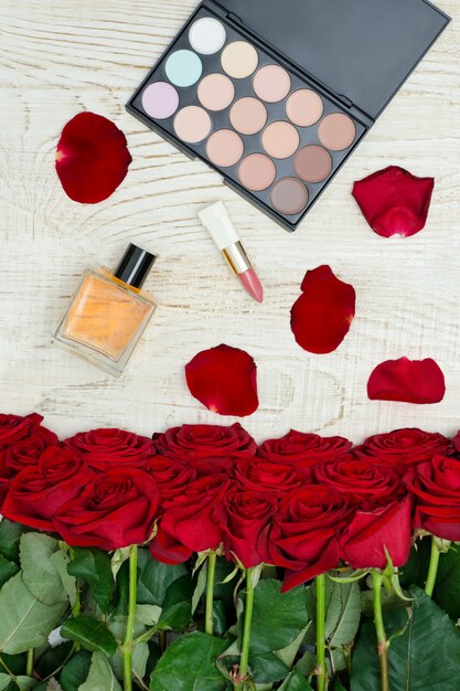 Bukiet czerwonych róż, perfum, szminki i palety cieni do powiek w