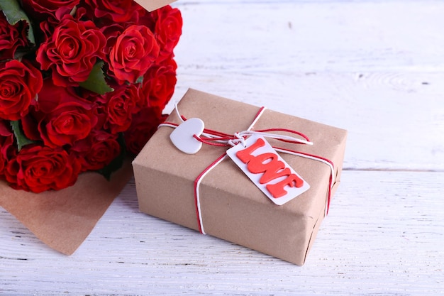 Bukiet czerwonych róż zawinięty w papier i obecne pudełko na drewnianym tle