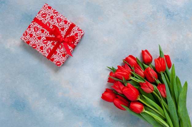 Bukiet czerwonych tulipanów i pudełko z czerwoną wstążką.