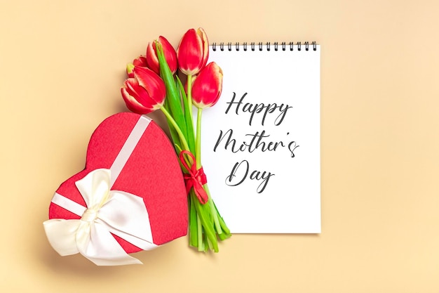 Bukiet czerwonych tulipanów tekst Happy Mother's Day na otwartym białym notatniku na beżowym tle