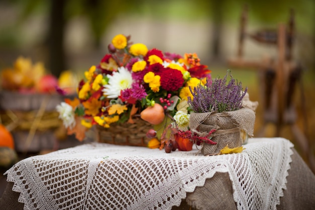 Bukiet jesiennych kwiatów w koszu na stole w stylu rustykalnym. Jesienny czas.