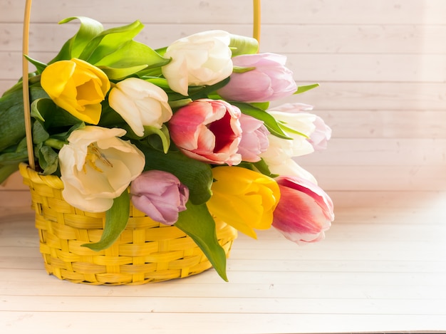 Bukiet kolorowych tulipanów w żółtym wiklinowym koszu.