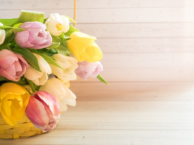 Bukiet kolorowych tulipanów w żółtym wiklinowym koszu.