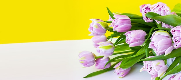 Bukiet kwiatów leży na białym stole. Fioletowe, niezwykłe tulipany liliowe z zielonymi liśćmi. Jasny szeroki baner i miejsce na tekst