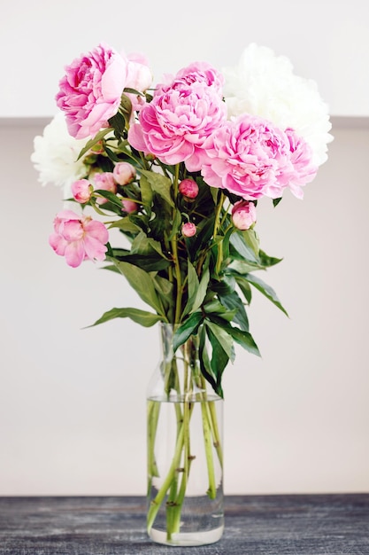 Bukiet kwiatów różowo-białych świeżych kwiatów piwonii w szklanym wazonie na stole