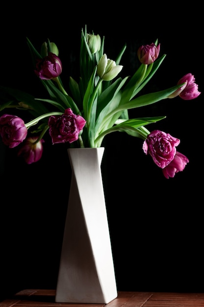 Bukiet pięknych różowych zielonych kwiatów tulipanów w białym wazonie na czarnym tle Niski klucz