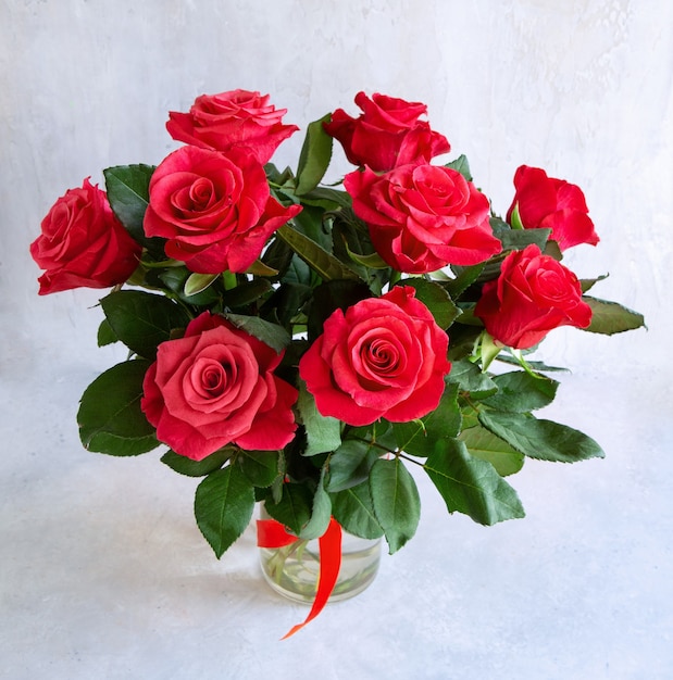 Zdjęcie bukiet przepięknych czerwonych róż w wazonie na jasnoszarym tle.