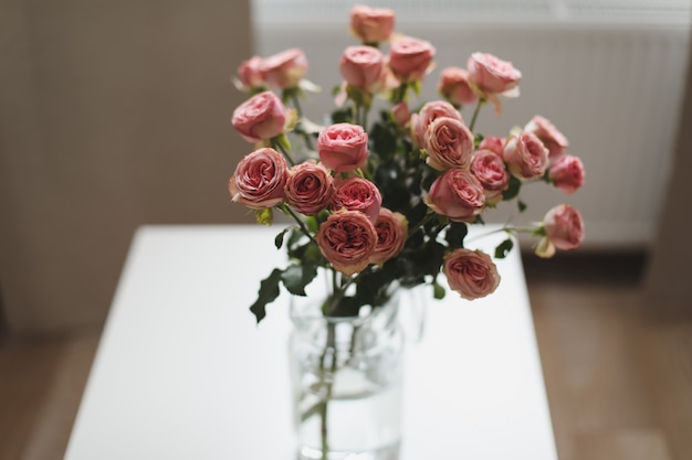 Bukiet różowych róż w szklanym wazonie przy oknie