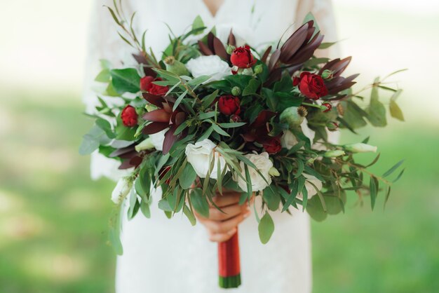 Bukiet ślubny z czerwonych kwiatów i zieleni w rękach Panny Młodej