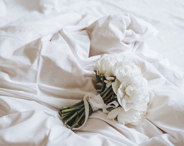 Bukiet ślubny z kwiatów piwonii na łóżku nowożeńców