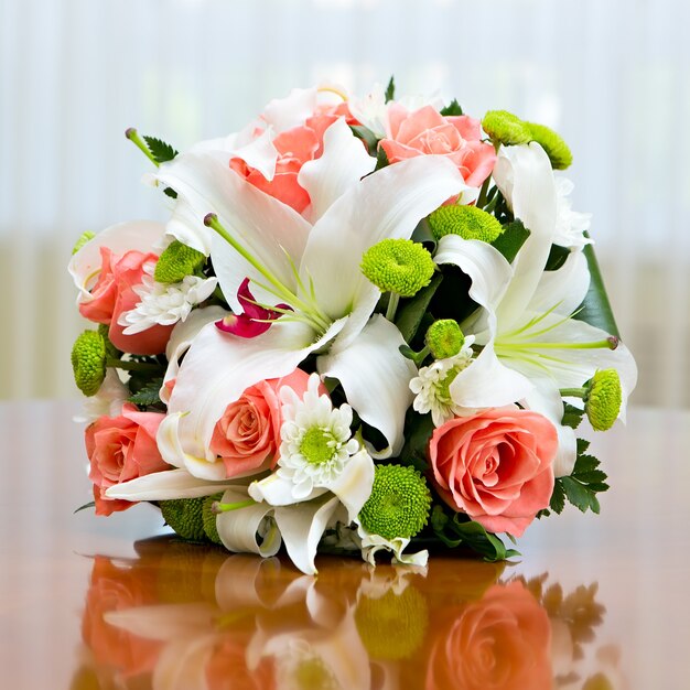 Bukiet ślubny z róż i lilii dla panny młodej na weselu. Bukiet ślubny z róż i lilii na stole na tle jasnego okna.