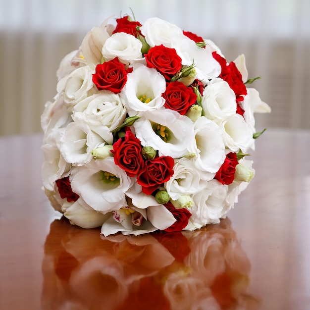 Bukiet ślubny z róż i lilii na stole na tle jasnego okna.