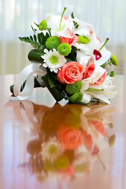 Bukiet ślubny z róż i lilii na stole na tle jasnego okna