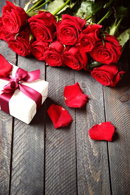 Bukiet świeżych czerwonych róż i obecne pudełko na drewnianym tle