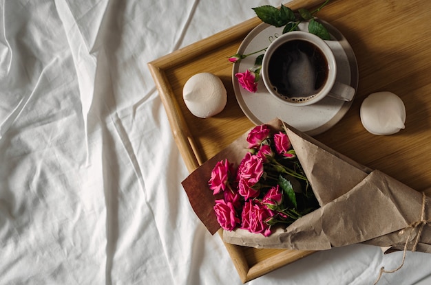 Zdjęcie bukiet wiosennych kwiatów i filiżankę kawy na drewnianej tacy w łóżku
