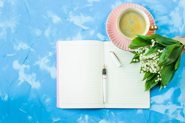 Bukiet z konwalii, filiżankę kawy i notatnik na niebieskim stole
