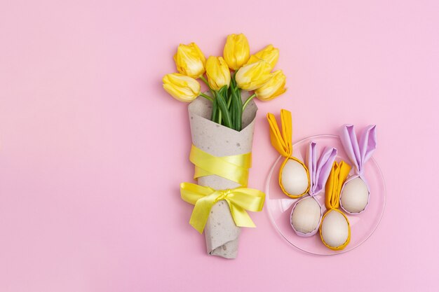 Bukiet żółci kwiaty tulipanowi i Easter jajka na talerzu, drewniani Easter jajka z tkanina ucho jak królik na menchiach z kopii przestrzenią. Leżał płasko, widok z góry.