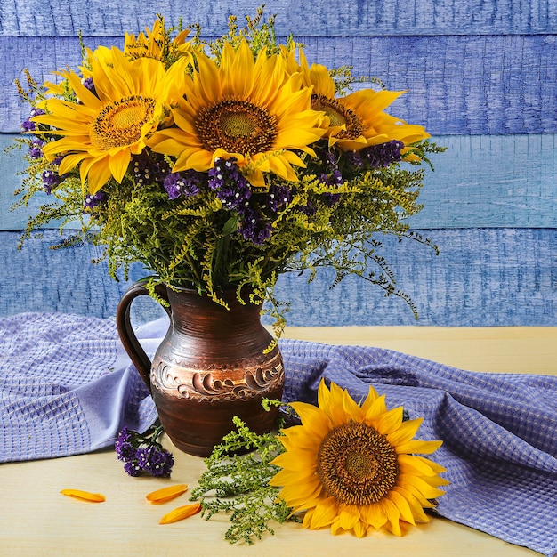 Zdjęcie bukiet żółtych słoneczników w glinianym dzbanku i suche kwiaty na niebieskim i żółtym tle