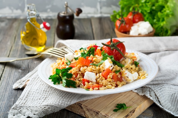 Bulgur z pieczoną papryką, pomidorami, pietruszką i serem feta na drewnianym tle. Selektywne ustawianie ostrości.