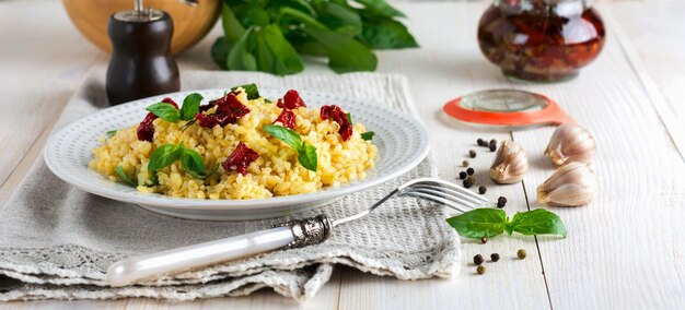 Bulgur z suszonymi pomidorami i bazylią na jasnym drewnianym tle. Danie wegetariańskie. Selektywne skupienie.