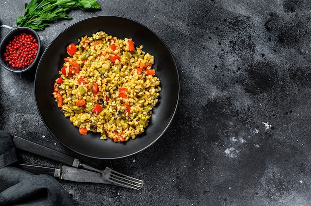 Bulgur z warzywami, cebulą, słodką papryką, marchewką i natką pietruszki w talerzu.