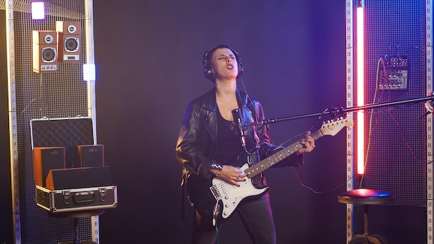 Buntowna, ostra kobieta grająca na gitarze w nowoczesnym studiu.
